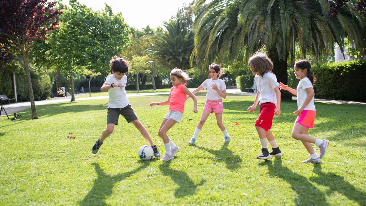 Group of kids enjoying a game of soccer in a lush green park on a sunny day in Portugal.